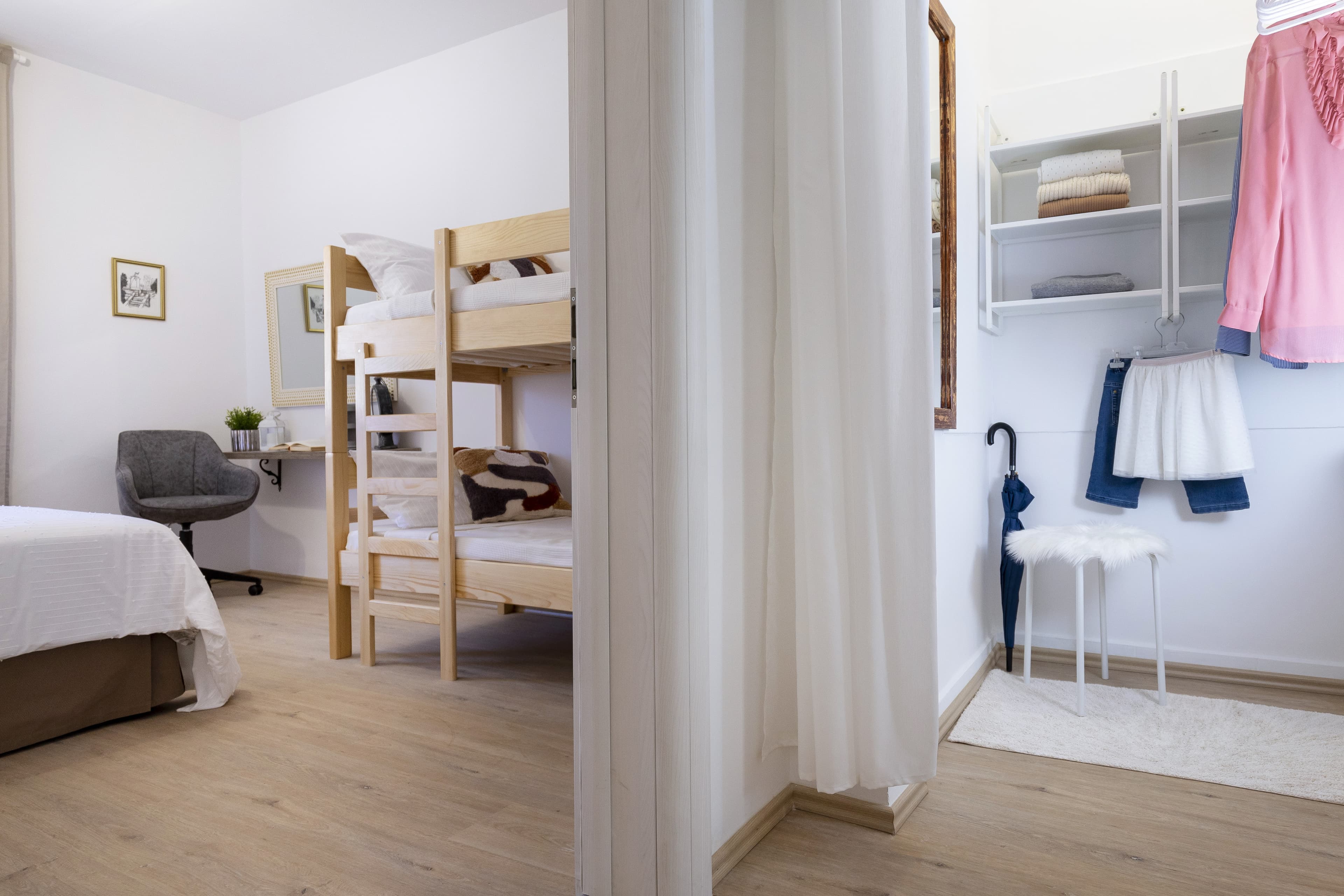 Minimalist bedroom with wooden bunk beds and an adjacent walk-in closet with white shelving.
