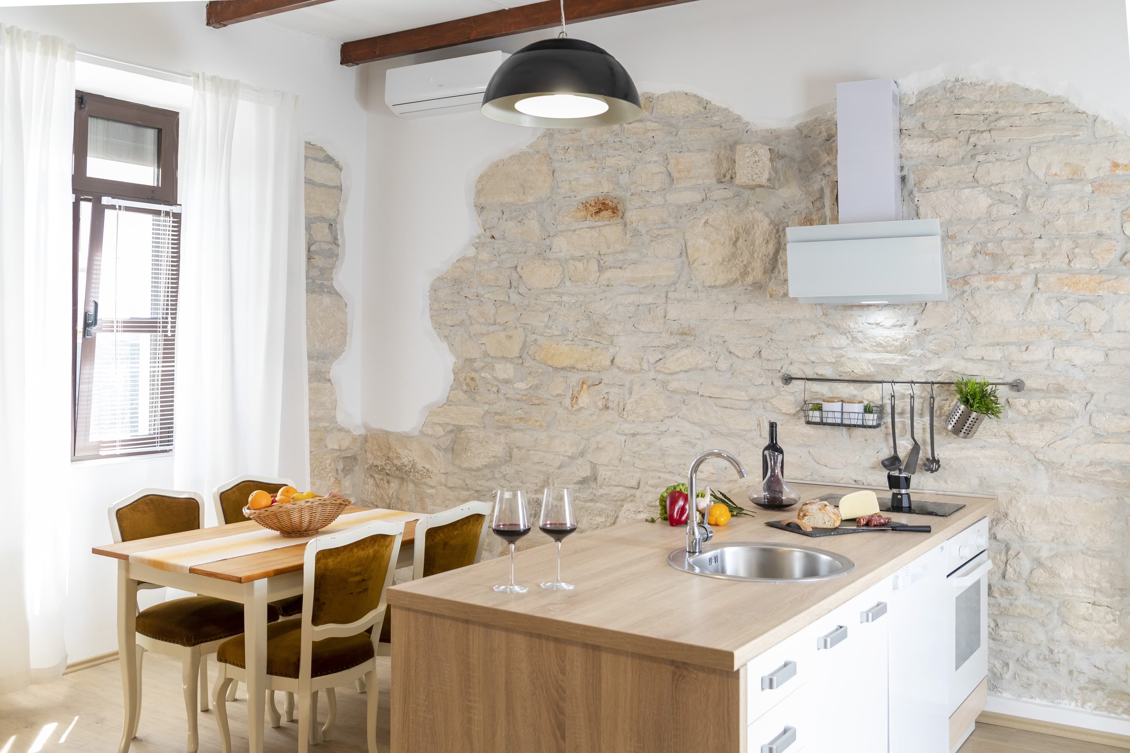 Modern kitchen featuring an exposed stone wall, wooden island with wine glasses, and dining area.
