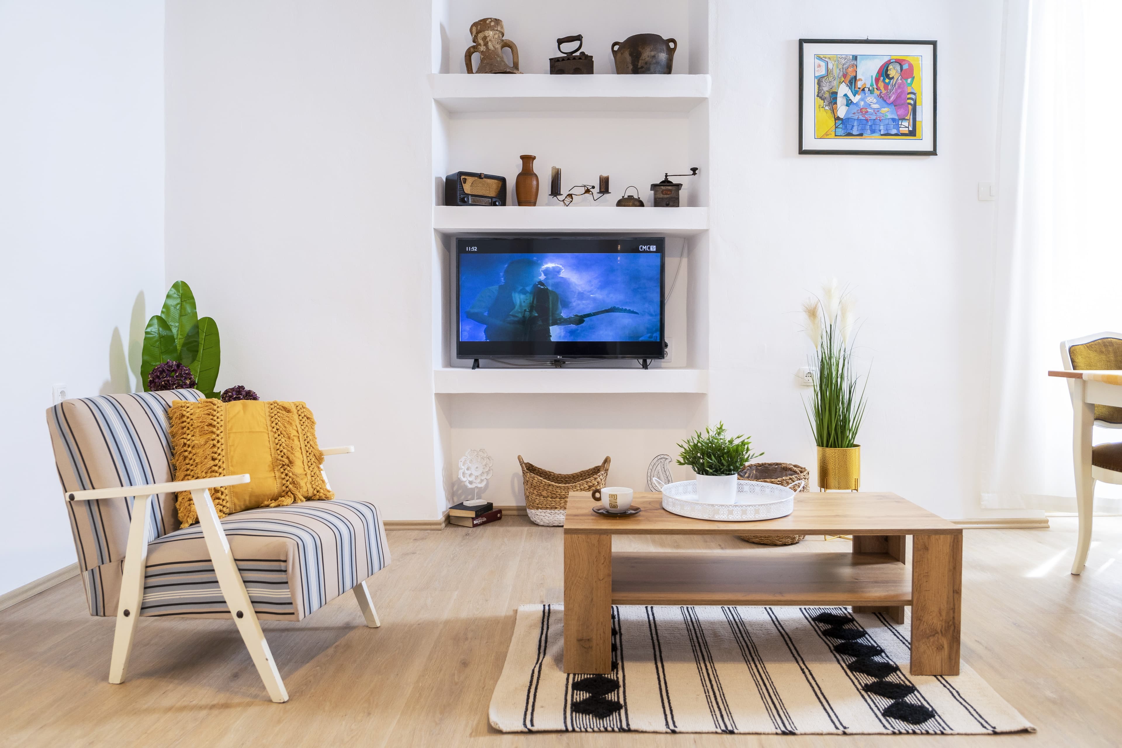 Bright living room with striped armchair, yellow pillow, and TV in built-in wall shelving.